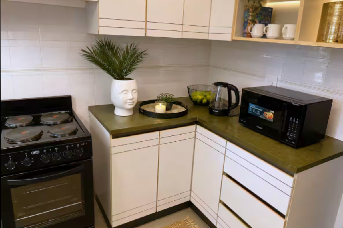 A compact kitchen featuring white cabinetry, a dark green countertop, tiled backsplash, and a freestanding electric stove with oven.