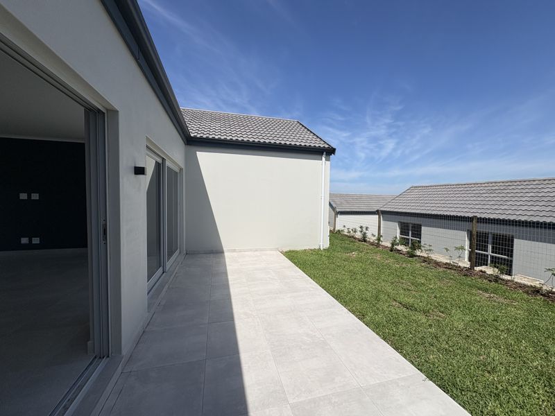A clean, modern tiled patio area leading from the interior living space, overlooking a well-maintained lawn and neighbouring cluster units.
