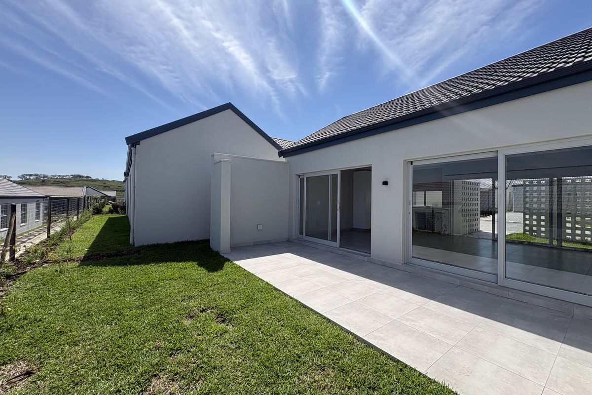A well-maintained rear exterior view featuring a paved patio, large sliding glass doors, and a neat lawn area.