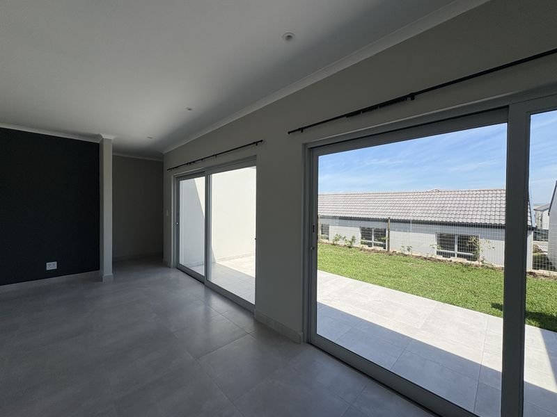 Spacious, modern living area featuring large sliding glass doors that open onto a paved patio and garden, finished with neutral tiles and downlights.