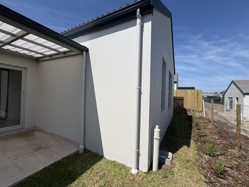 A view of the rear exterior featuring a covered patio with tiled flooring, sliding glass doors, and well-maintained plastered walls.