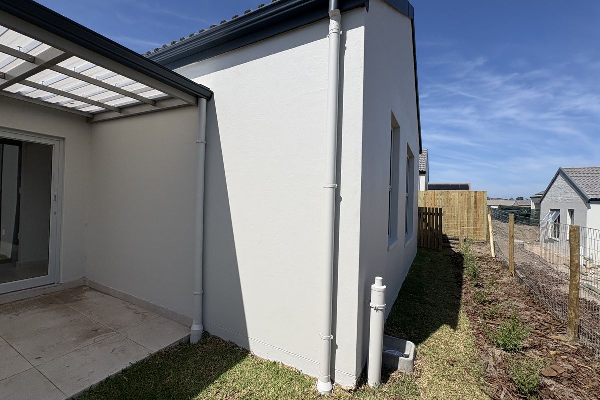 A view of the rear exterior featuring a covered patio with tiled flooring, sliding glass doors, and well-maintained plastered walls.