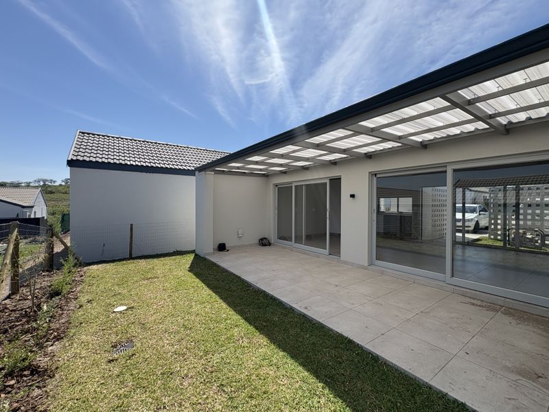A modern covered patio featuring tiled flooring and a translucent roof, providing seamless indoor-outdoor flow through large sliding glass doors to the garden.