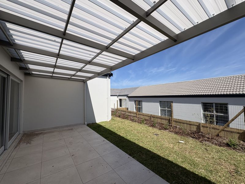 A covered patio area with tiled flooring and a translucent roof, leading out to a small private garden space.