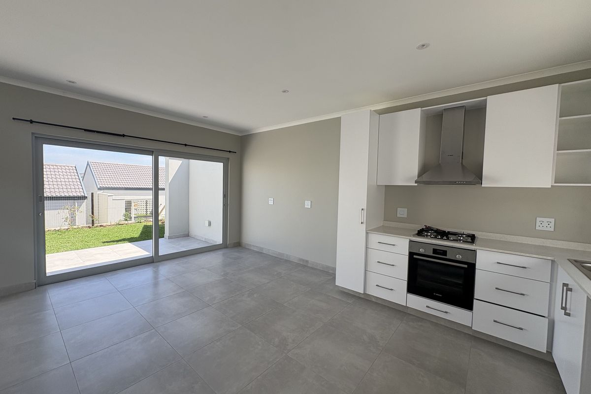 Modern open-plan kitchen and living area featuring sleek white cabinetry, integrated appliances, large format floor tiles, and seamless access to a private patio.