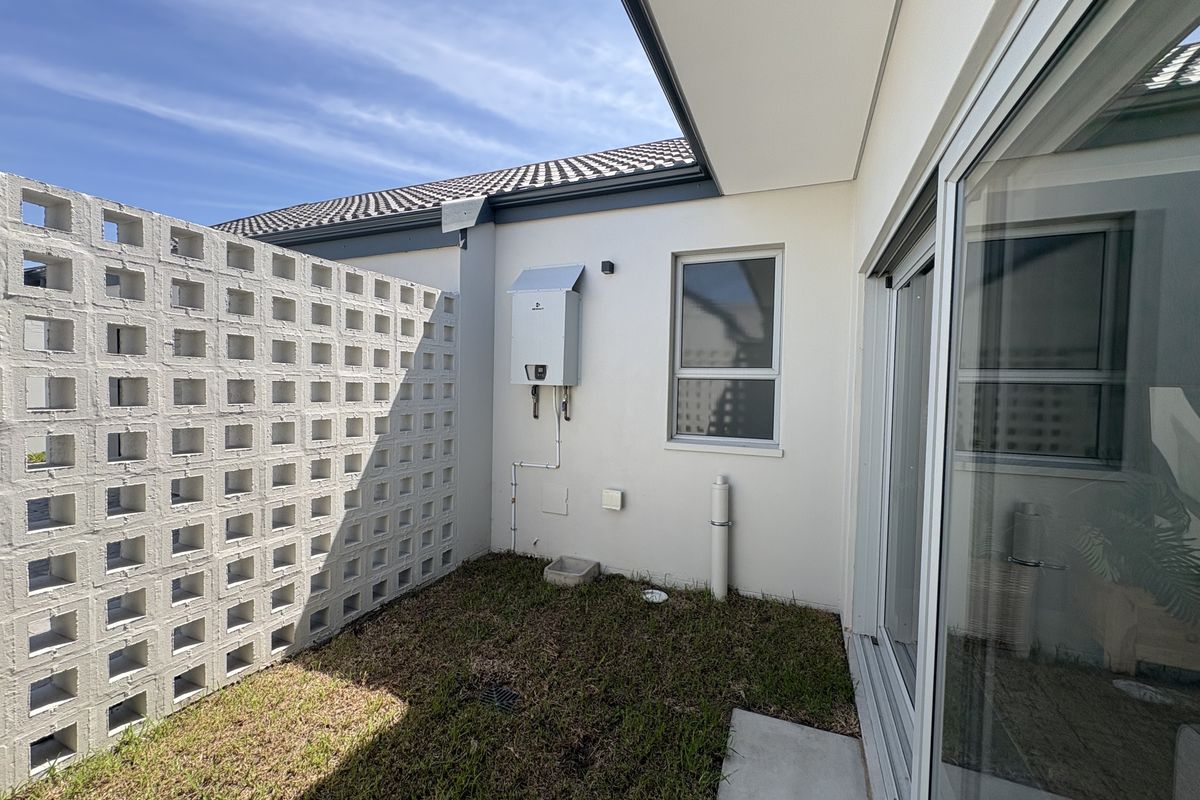 A private rear courtyard area featuring a breeze block boundary wall, a wall-mounted gas geyser, and access via a large sliding glass door.
