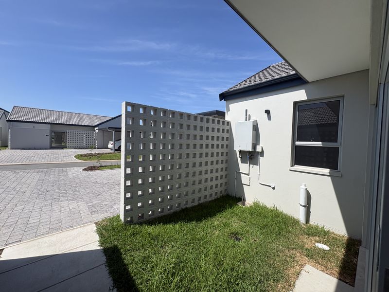 A view of the front exterior area featuring a decorative breeze block privacy screen, paved driveway, and well-maintained lawn.