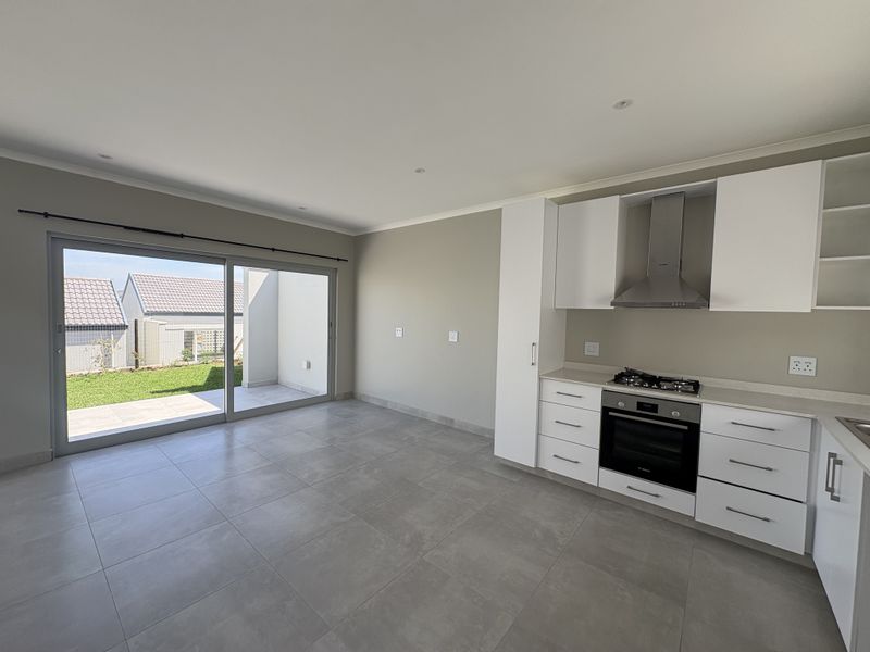 Modern open-plan kitchen and living area featuring sleek white cabinetry, integrated appliances, large format floor tiles, and seamless access to a private patio.