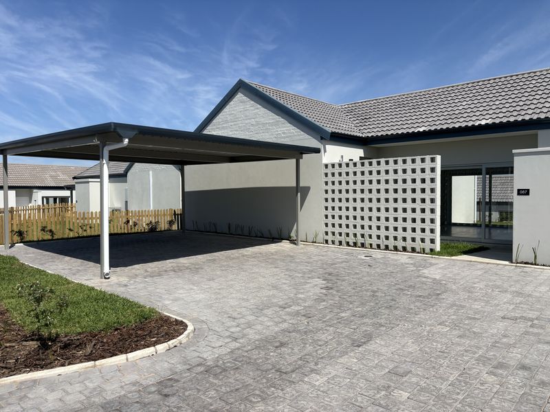 Modern cluster home exterior featuring a paved driveway, a functional carport, and a decorative breeze block privacy screen.