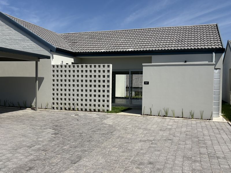 Modern cluster home exterior featuring a paved driveway, carport, decorative breeze block wall, and a clean, well-maintained facade.