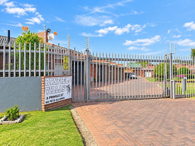 Front entrance view of Rynfield Villas featuring a secure metal gate, electric fencing, and brick paved driveway access.
