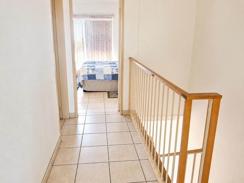 A bright upstairs hallway featuring tiled flooring and a timber and metal balustrade overlooking the staircase, leading into a bedroom.