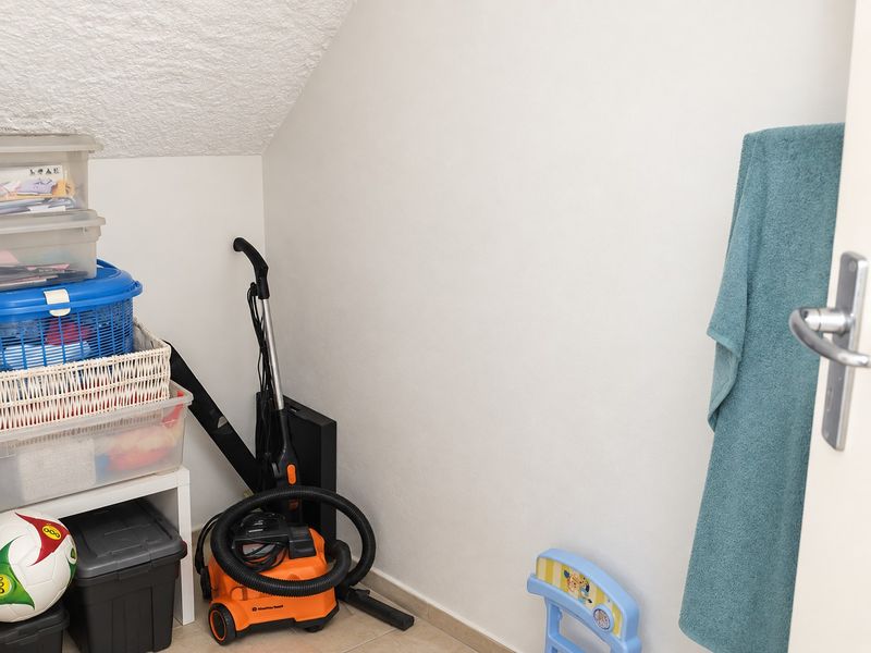 A small utility storage space featuring a sloped ceiling and tiled flooring, currently used for household storage.