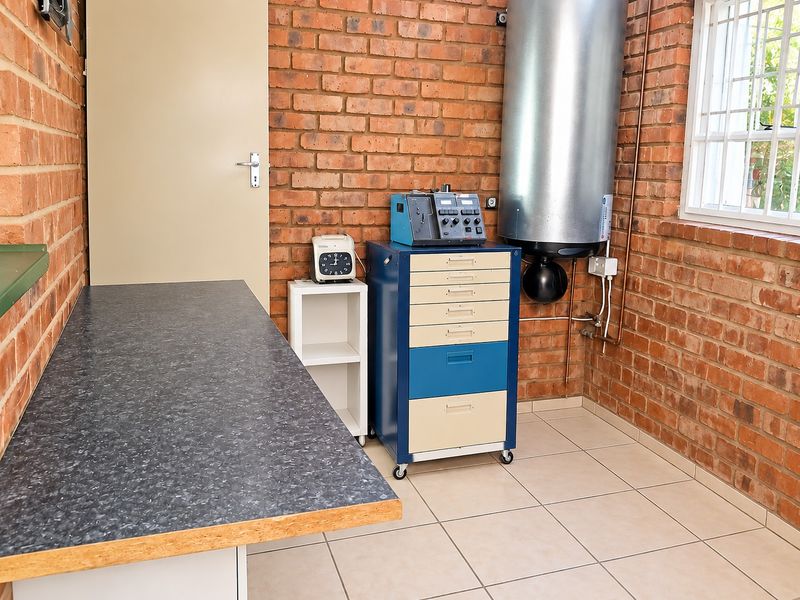 A functional utility space featuring exposed brick walls, tiled flooring, and a wall-mounted geyser, providing practical storage and workspace.