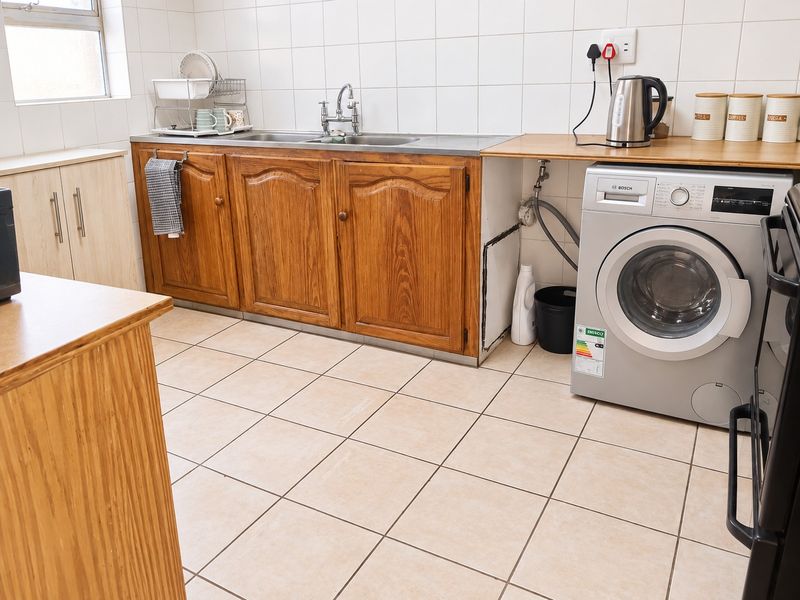 A functional kitchen featuring wooden cabinetry, tiled splashbacks, tiled flooring, and dedicated space for a washing machine with integrated plumbing connections.