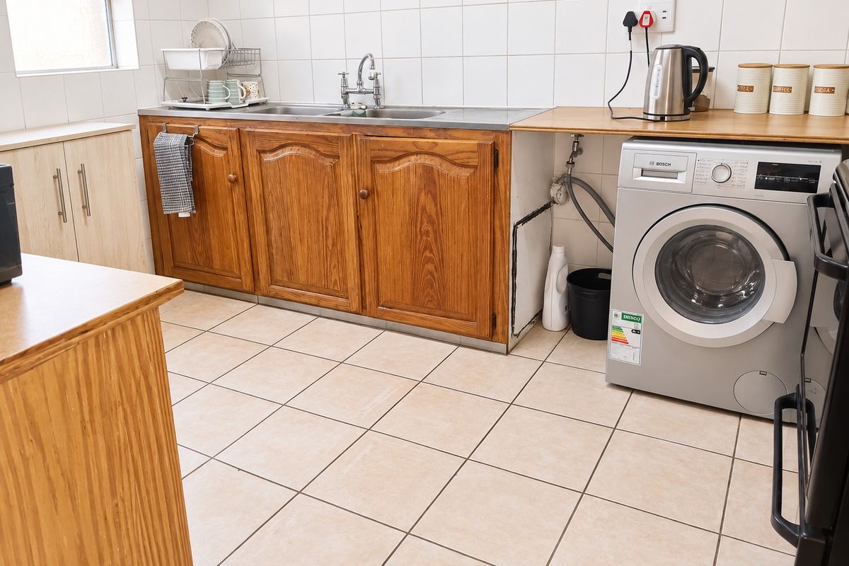 A functional kitchen featuring wooden cabinetry, tiled splashbacks, tiled flooring, and dedicated space for a washing machine with integrated plumbing connections.