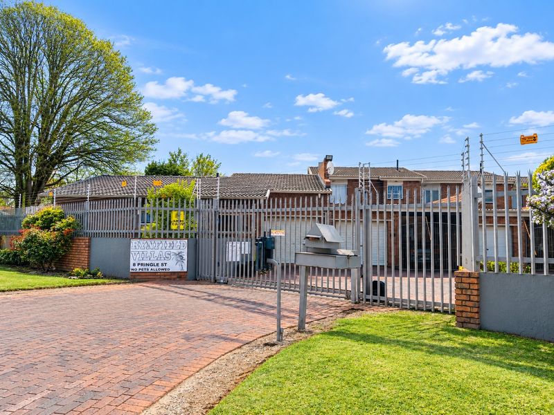 Front entrance view of Rynfield Villas featuring a secure gated access point, brick driveway, and perimeter electric fencing.