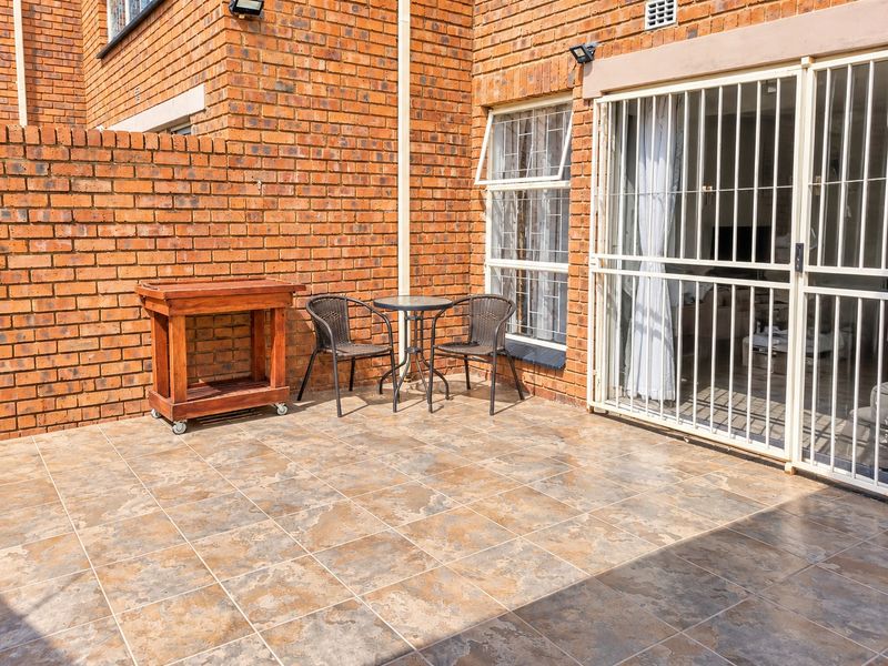 A private outdoor patio area featuring durable tiled flooring, exposed brick walls, and secure sliding door access with fitted security bars.