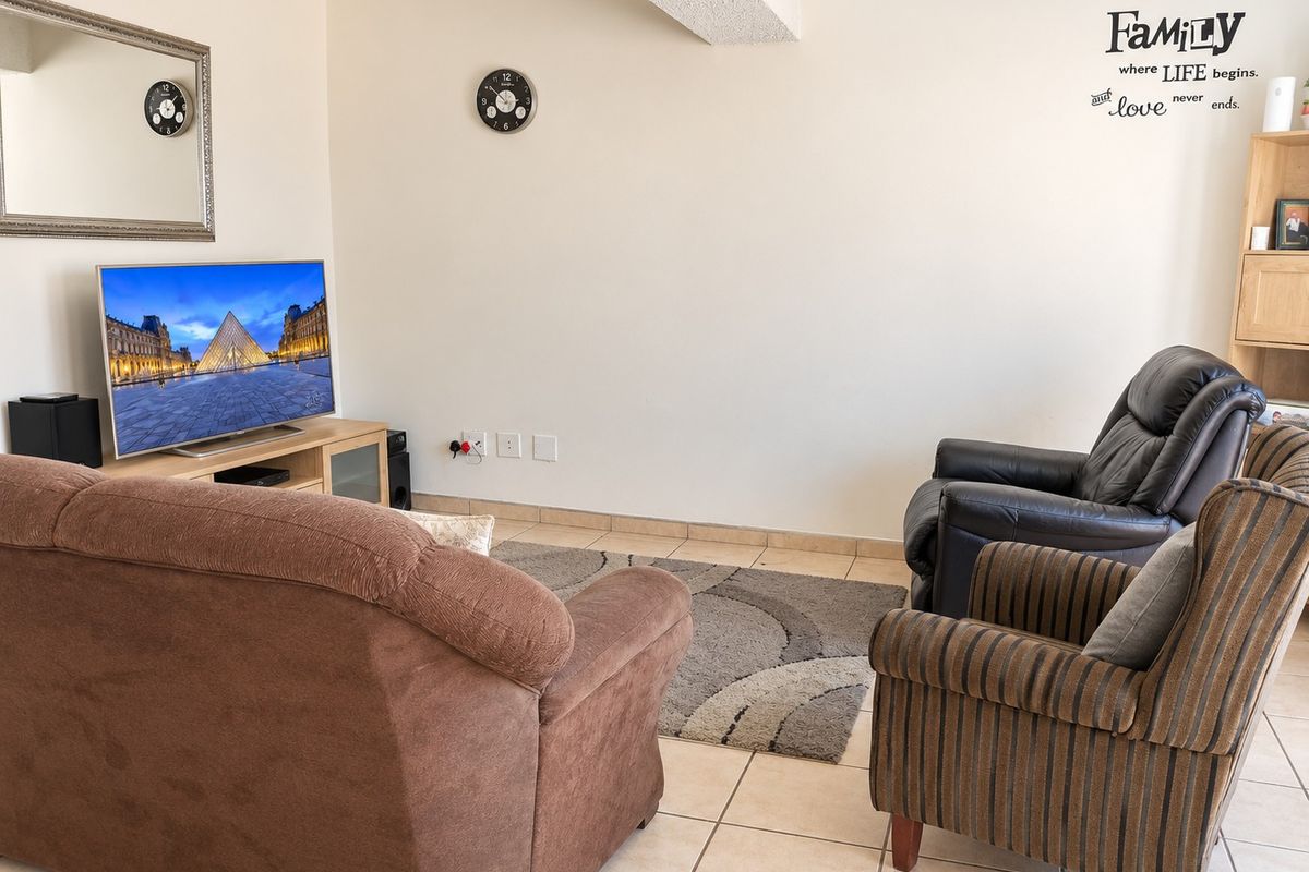 A functional living room featuring tiled flooring and a textured ceiling beam, providing a neutral base for interior updates.
