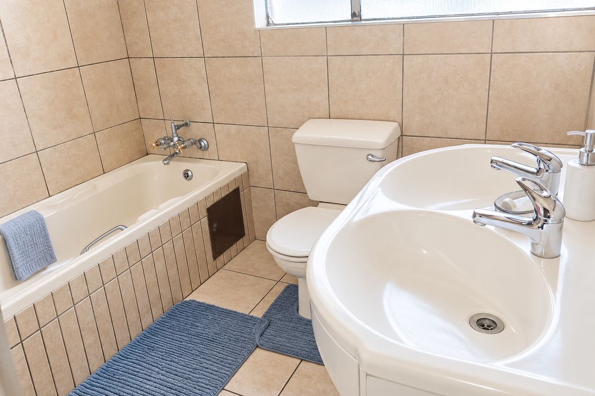 A functional bathroom featuring a bathtub, toilet, and a double vanity with chrome fixtures, finished with neutral wall and floor tiling.