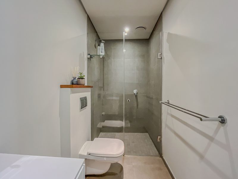 Modern bathroom featuring a wall-hung toilet, a glass-enclosed walk-in shower with tiled finishes, and a sleek towel rail.