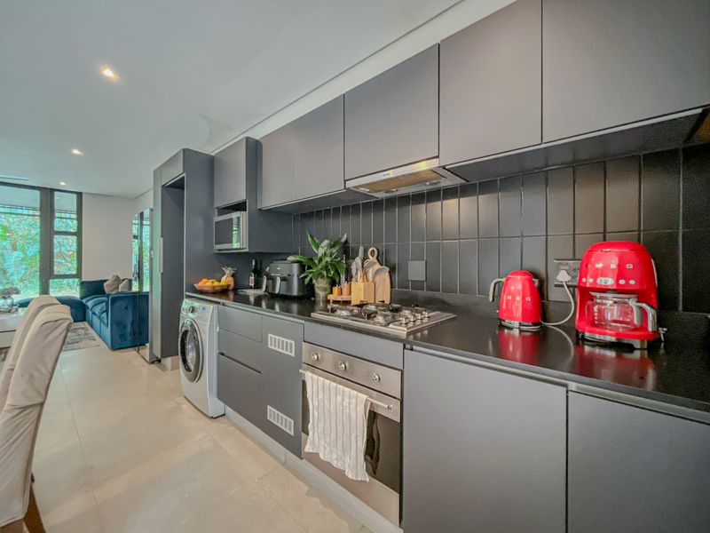 Modern open-plan kitchen featuring dark matte cabinetry, integrated appliances, gas hob, and tiled splashback, seamlessly flowing into the adjacent living area.