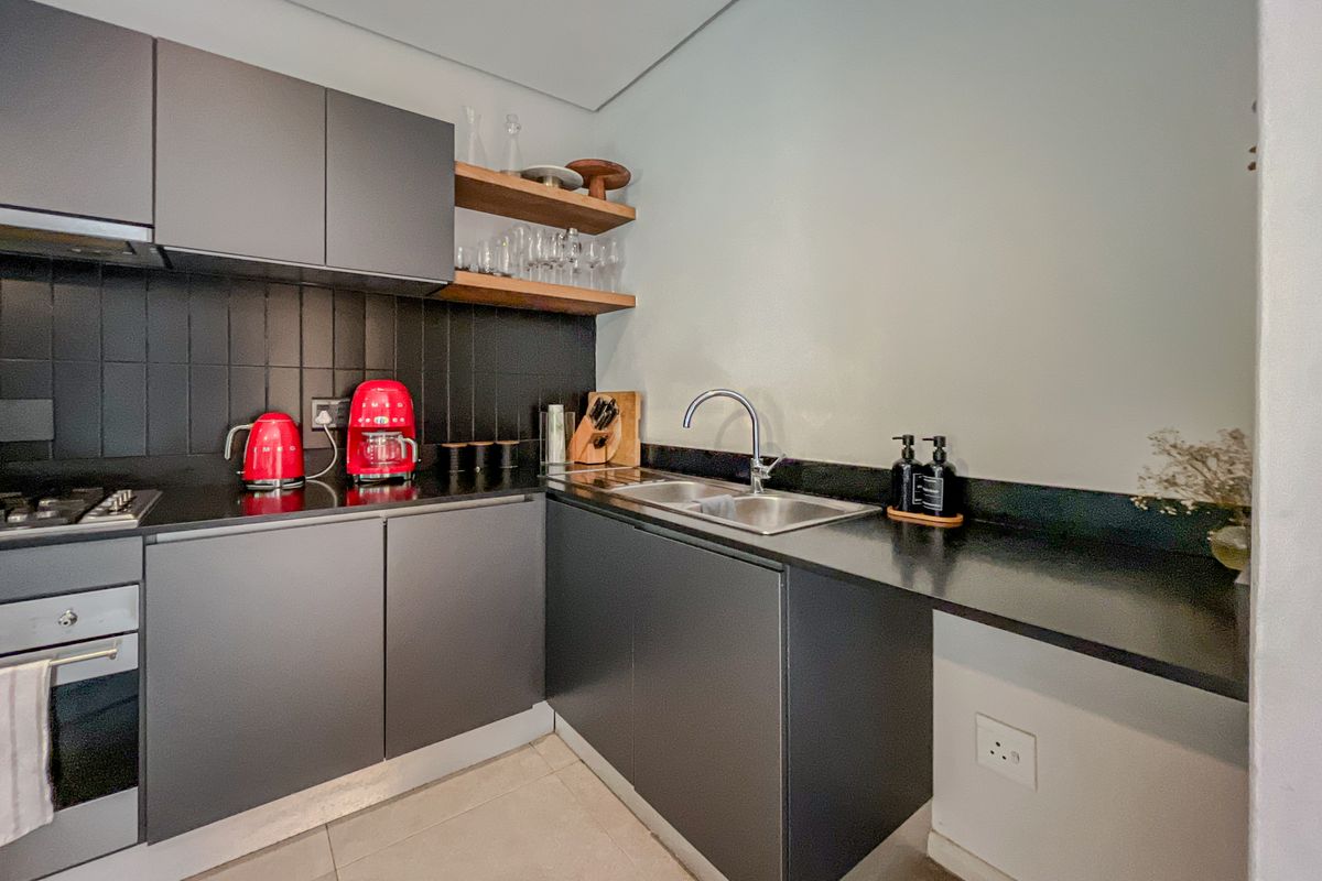 Modern kitchen featuring sleek dark cabinetry, stone countertops, integrated stainless steel sink, built-in oven, gas hob, and stylish floating timber shelving.