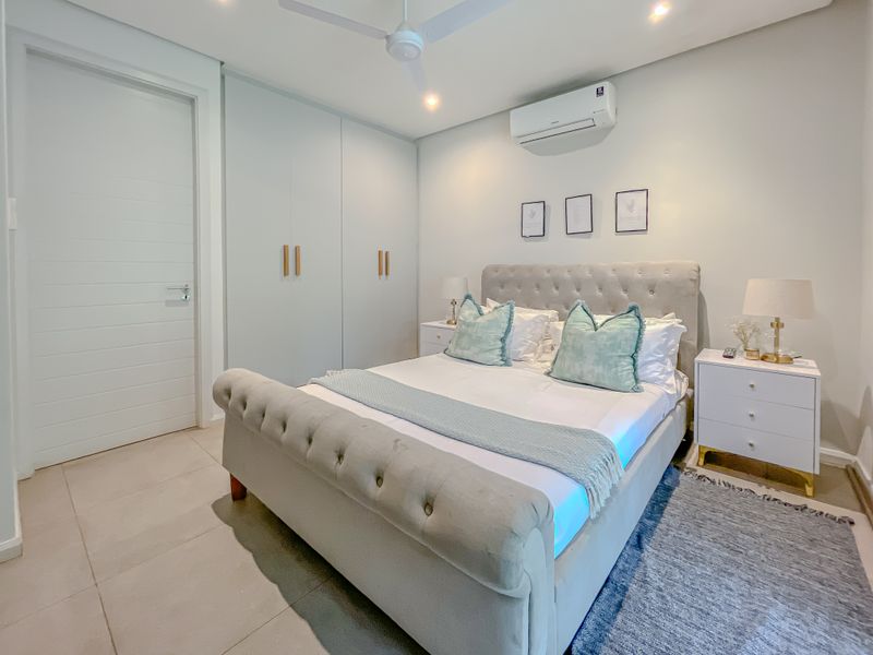 A well-maintained bedroom featuring built-in cupboards, a split-system air conditioner, ceiling fan, and neutral tiled flooring.