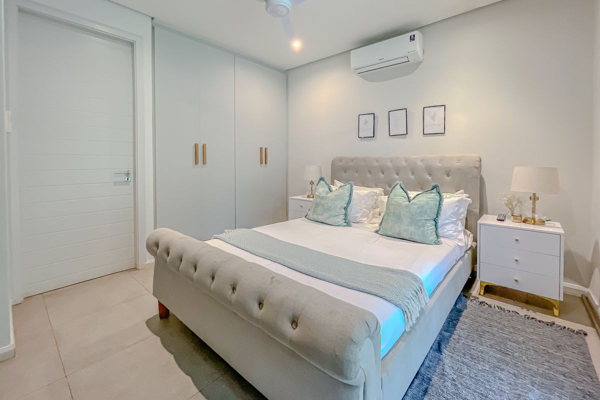 A well-maintained bedroom featuring built-in cupboards, a split-system air conditioner, ceiling fan, and neutral tiled flooring.