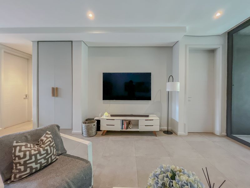 A modern, well-maintained living room featuring neutral tiled flooring, recessed ceiling lighting, and clean, minimalist built-in cabinetry.