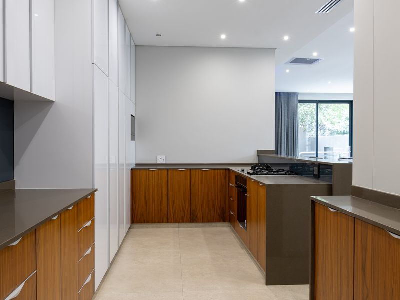 Modern kitchen featuring sleek wood-grain and white cabinetry, stone countertops, integrated gas hob, and built-in oven in a clean, contemporary layout.
