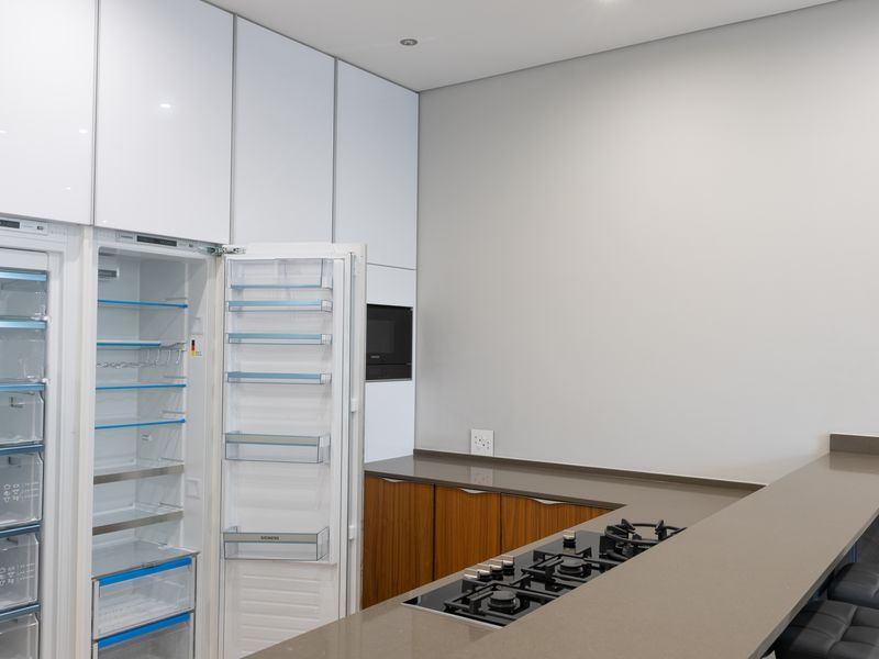 Modern kitchen featuring high-gloss white cabinetry, integrated refrigerator, stone countertops, and a gas hob with an attached breakfast bar.