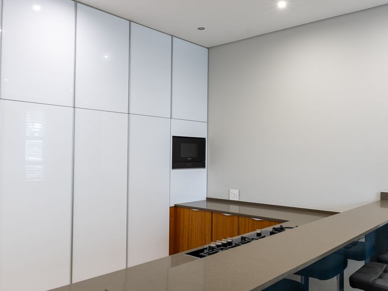 Modern kitchen featuring sleek white floor-to-ceiling cabinetry, wood-finish lower cabinets, stone countertops, and a built-in gas hob and microwave.