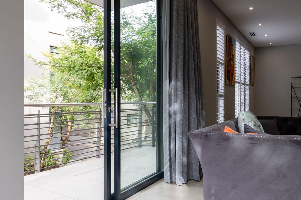 Modern living area featuring large sliding glass doors opening onto a private balcony with metal railings and recessed ceiling lighting.