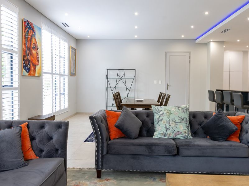 Spacious open-plan living and dining area featuring modern recessed downlighting, cove lighting, and plantation shutters, seamlessly connecting to a contemporary kitchen.
