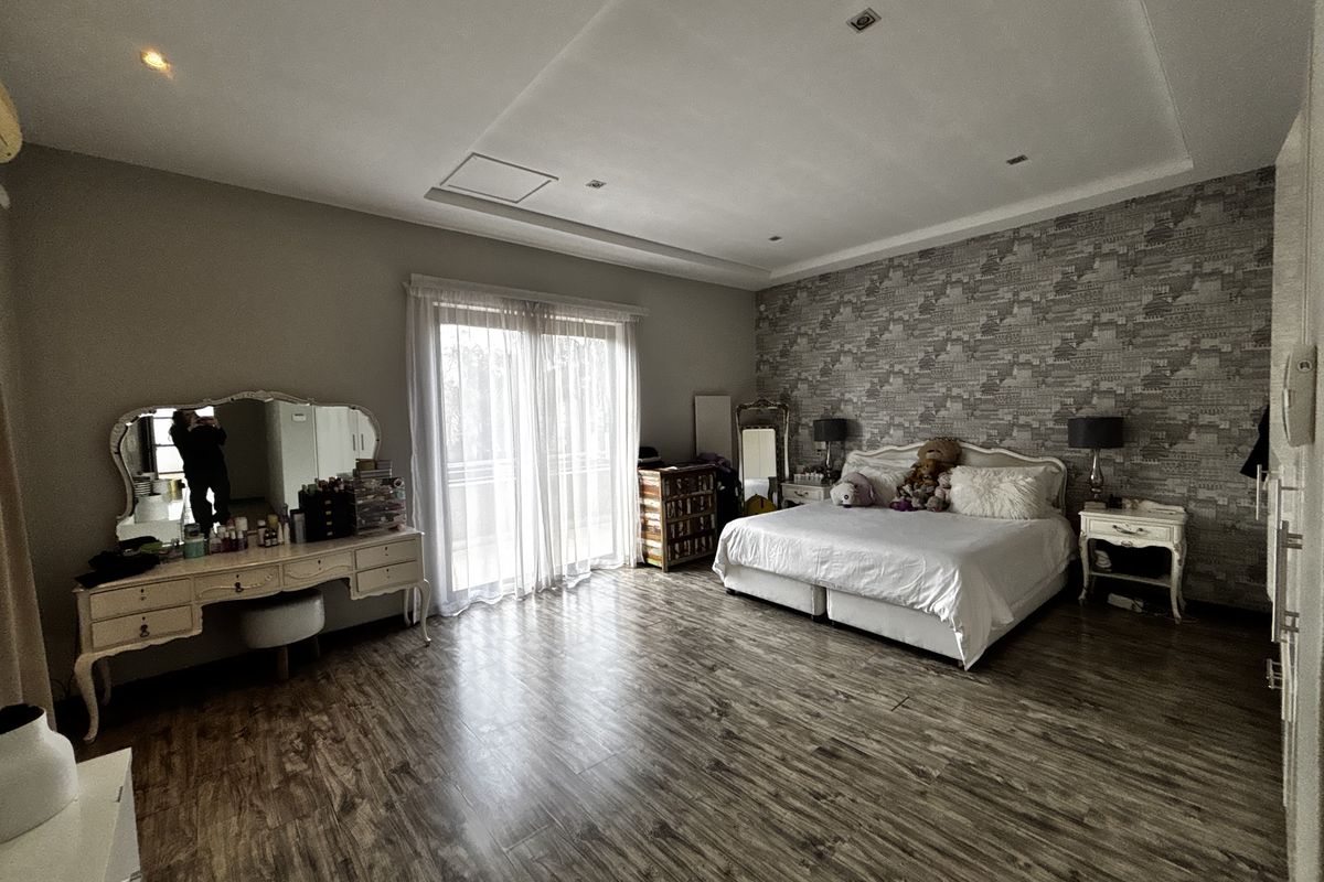 Spacious bedroom featuring laminate flooring, recessed ceiling lighting, a feature wallpaper wall, and sliding glass doors leading to a balcony.