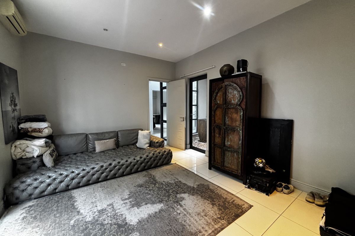 A living room featuring neutral tiled flooring, recessed lighting, and an integrated air conditioning unit, with access to an outdoor area through a glass door.