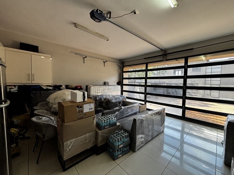 A spacious garage featuring tiled flooring, built-in storage cabinetry, and an automated sectional garage door with a motor mechanism.