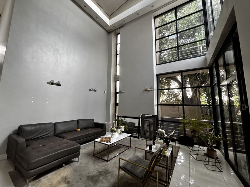 Spacious double-volume living room featuring expansive black-framed windows, high ceilings with recessed lighting, and modern tiled flooring.