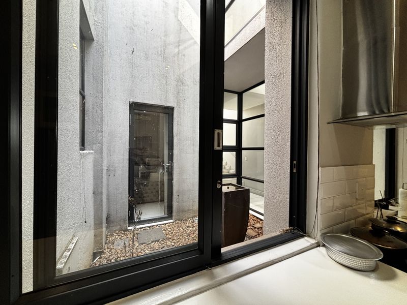 Kitchen view looking out onto a private internal courtyard with pebble landscaping and modern sliding window frame.
