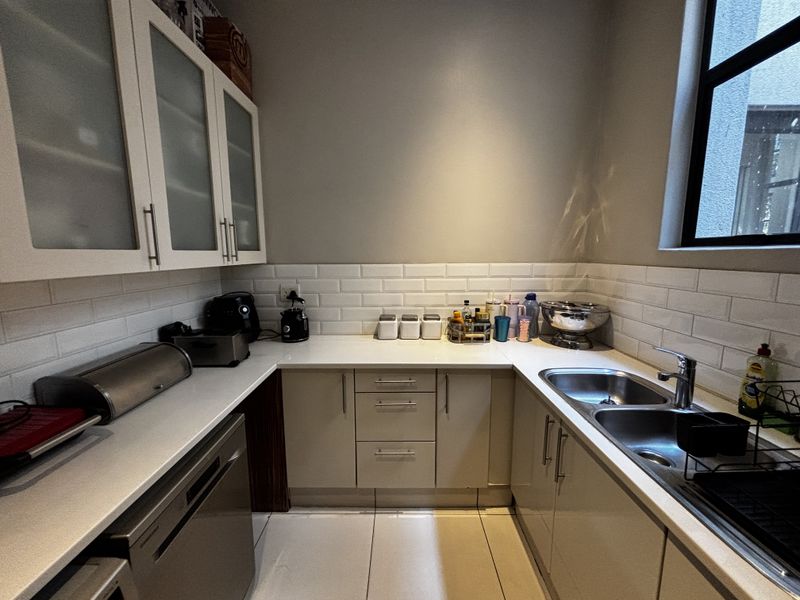 A functional scullery featuring white subway tile backsplash, double basin sink, ample cabinetry, and stone countertops, providing efficient workspace for food preparation and cleaning.
