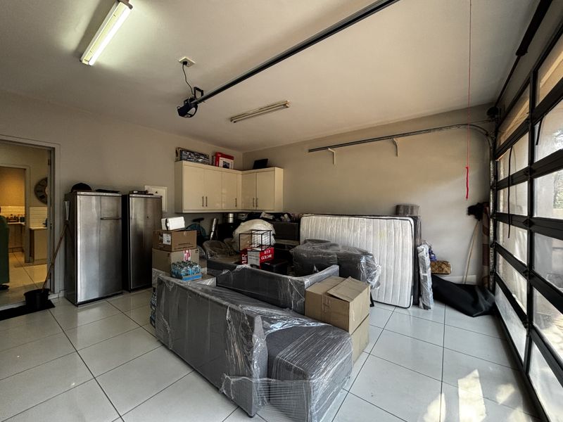 A spacious garage featuring tiled flooring, built-in storage cabinetry, and an automated door mechanism, providing ample space for vehicle parking and additional storage.