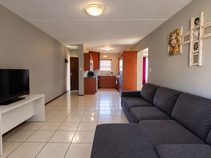 Open-plan living area featuring tiled floors and a functional kitchen with wood-finish cabinetry, seamlessly connecting the lounge and kitchen spaces.