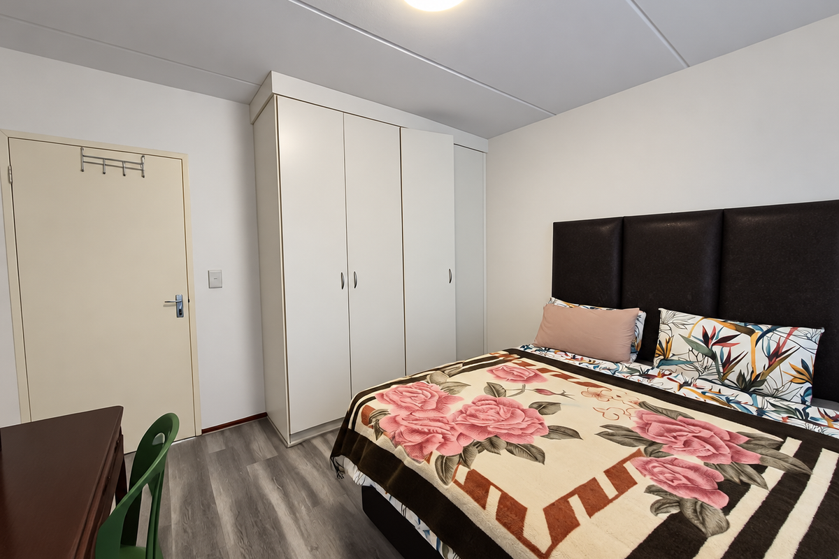 A well-maintained bedroom featuring modern laminate flooring, neutral walls, and a spacious built-in wardrobe providing ample storage.