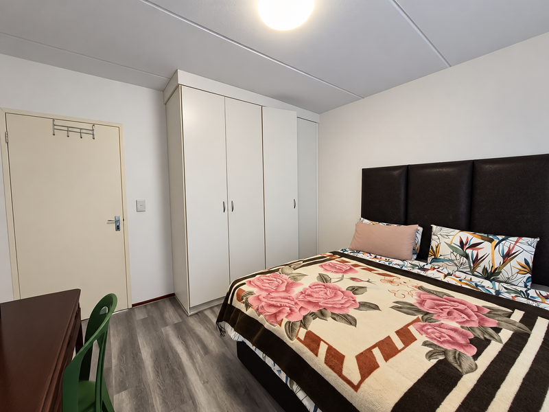 A well-maintained bedroom featuring modern laminate flooring, neutral walls, and a spacious built-in wardrobe providing ample storage.