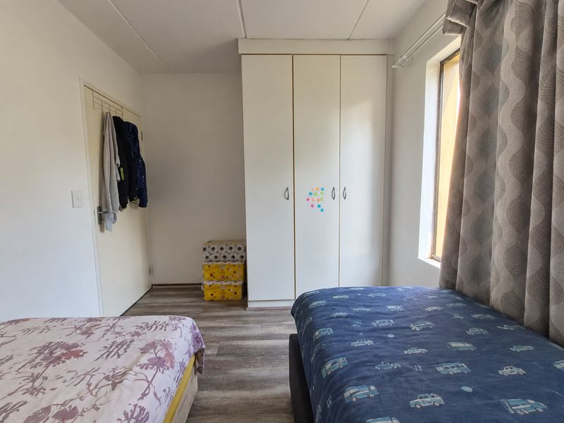 A functional bedroom featuring built-in wardrobes and durable laminate flooring, providing a practical space with natural light.