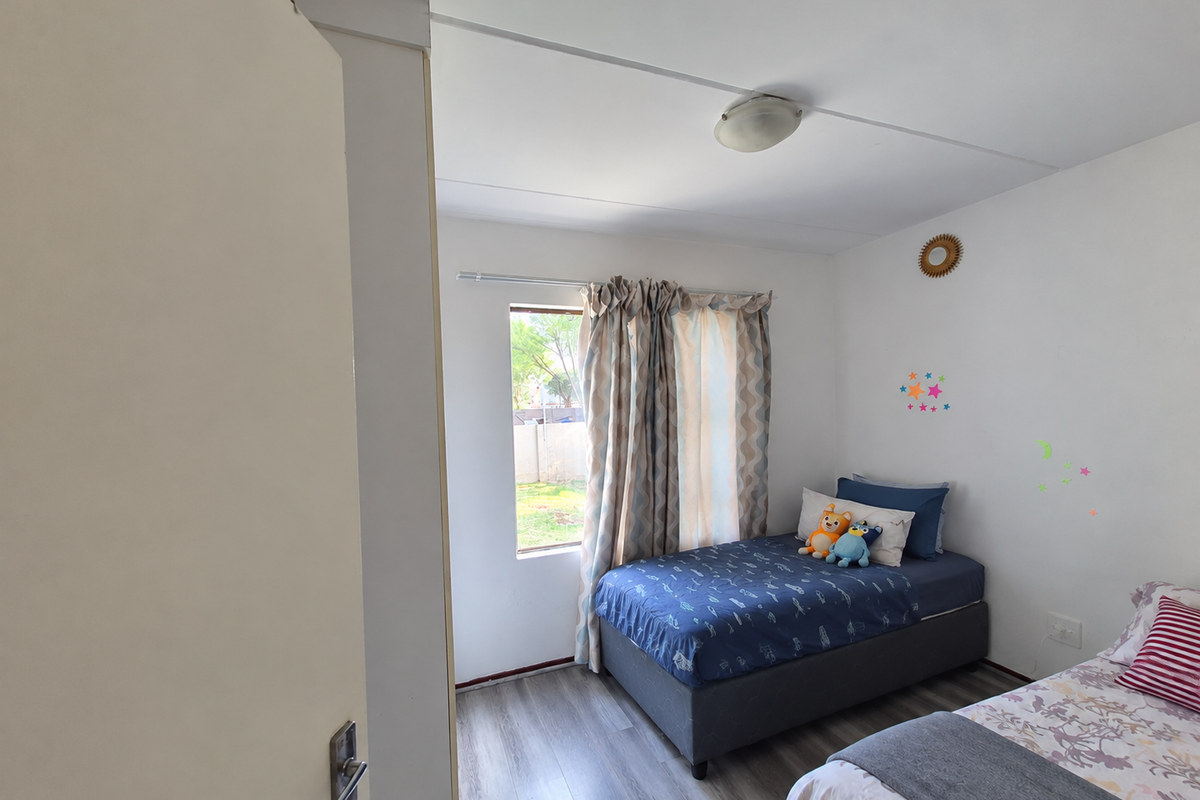 A bedroom featuring laminate flooring, a central ceiling light, and a window with curtains, providing natural light to the space.