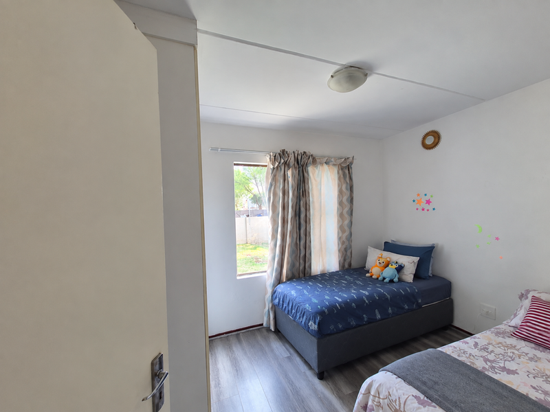 A bedroom featuring laminate flooring, a central ceiling light, and a window with curtains, providing natural light to the space.