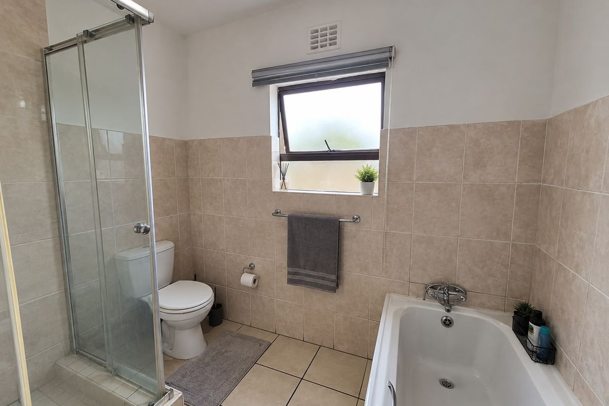 A clean, functional bathroom featuring a glass-enclosed shower, a bathtub, and neutral wall and floor tiling.