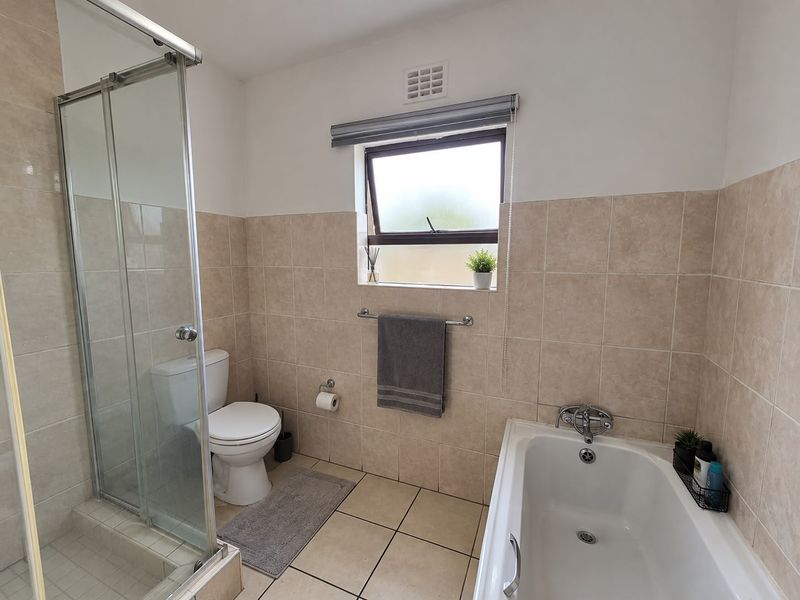 A clean, functional bathroom featuring a glass-enclosed shower, a bathtub, and neutral wall and floor tiling.